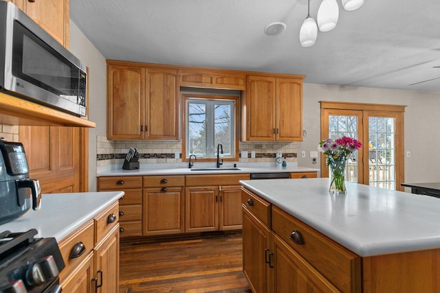 kitchen with a sink, light countertops, dark wood-style floors, stainless steel microwave, and decorative backsplash