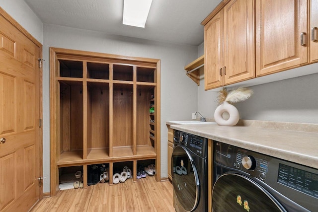 laundry area featuring light wood-style floors, separate washer and dryer, a sink, and cabinet space