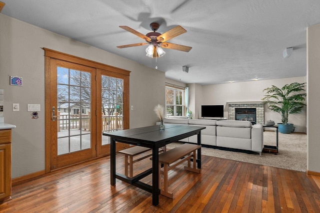 dining area with hardwood / wood-style floors, ceiling fan, baseboards, and a glass covered fireplace