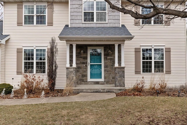 doorway to property with roof with shingles, stone siding, and a lawn