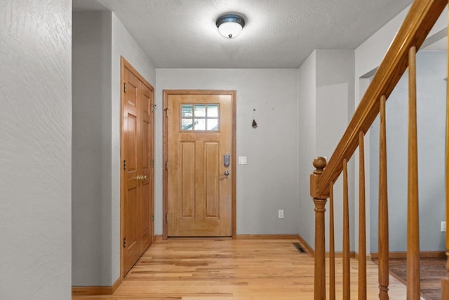 foyer with visible vents, light wood-type flooring, stairway, and a textured ceiling