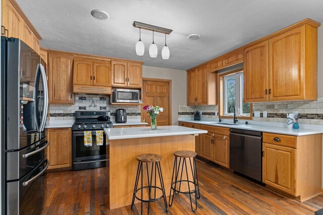 kitchen with dark wood-type flooring, a kitchen island, appliances with stainless steel finishes, a sink, and light countertops
