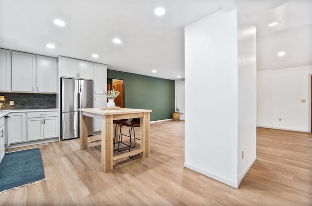 kitchen with light wood-style flooring, tasteful backsplash, baseboards, and stainless steel fridge