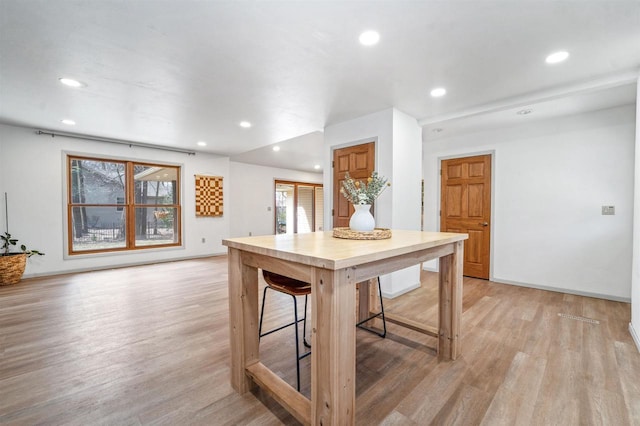 kitchen featuring baseboards, light wood-type flooring, a kitchen bar, and recessed lighting
