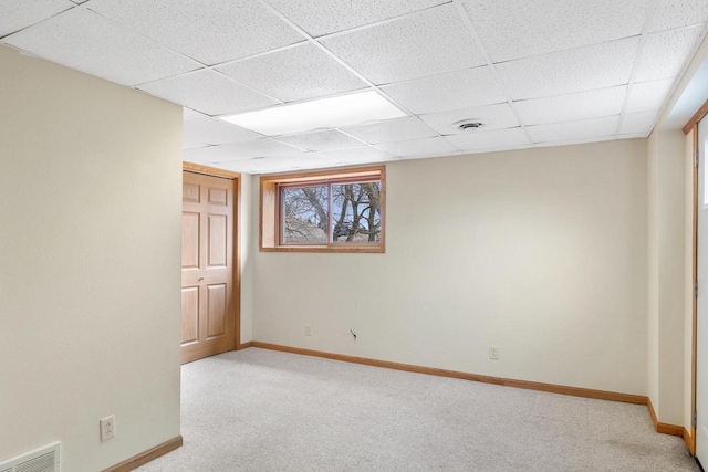 below grade area featuring a paneled ceiling, visible vents, light colored carpet, and baseboards