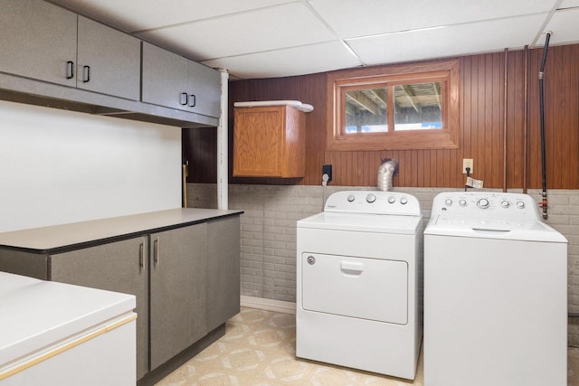 laundry room with independent washer and dryer, wooden walls, cabinet space, and light floors