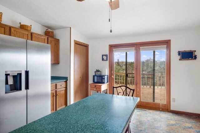 kitchen featuring baseboards, stainless steel refrigerator with ice dispenser, a ceiling fan, brown cabinetry, and black microwave