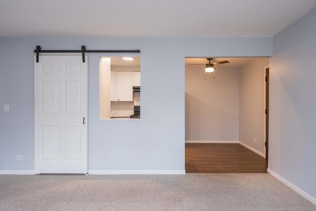 unfurnished room with a barn door, carpet, baseboards, and ceiling fan