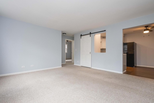 carpeted empty room featuring baseboards and a barn door