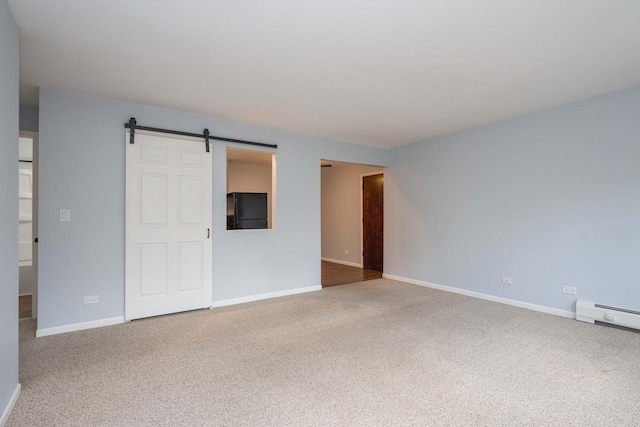 carpeted spare room featuring baseboards, a barn door, and baseboard heating