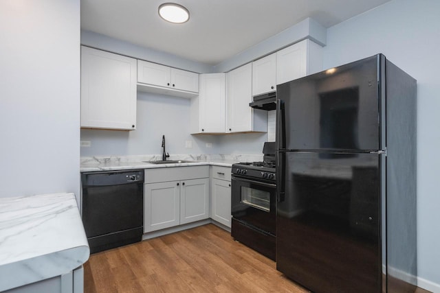 kitchen with white cabinets, a sink, under cabinet range hood, black appliances, and wood finished floors