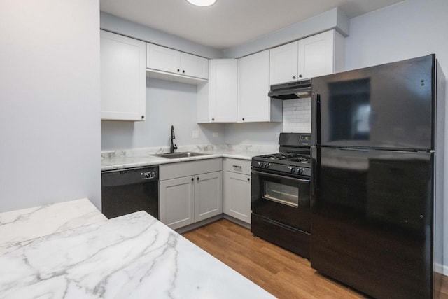 kitchen with a sink, under cabinet range hood, black appliances, wood finished floors, and light stone counters