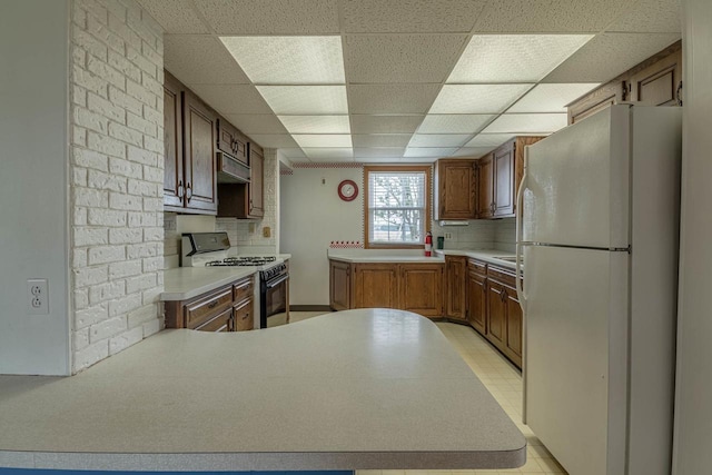 N1616 Haddinger Rd, Monroe, WI 53566 - kitchen with freestanding refrigerator, gas range, under cabinet range hood, a peninsula, and a drop ceiling