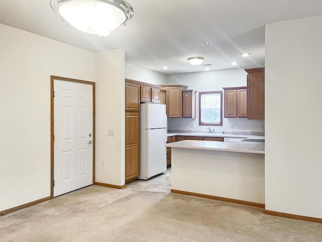 kitchen featuring freestanding refrigerator, a peninsula, light colored carpet, light countertops, and a sink