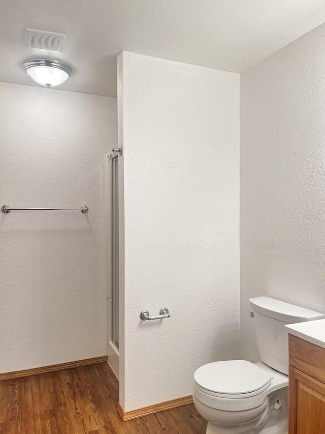 bathroom with vanity, toilet, visible vents, a shower with shower door, and wood finished floors