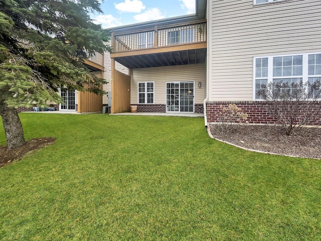back of property featuring a yard, brick siding, and a balcony