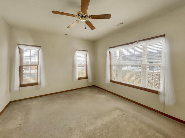 carpeted spare room with visible vents, baseboards, and a ceiling fan