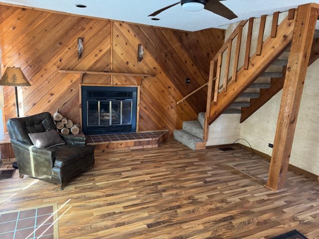 interior space with a tiled fireplace, a ceiling fan, stairway, wood finished floors, and wood walls
