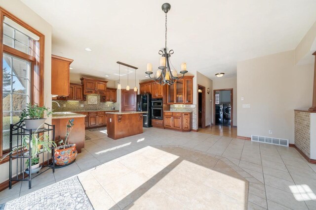 3895 Shorebird Ct, Oshkosh, WI 54904 - kitchen with a notable chandelier, visible vents, independent washer and dryer, brown cabinetry, and black appliances