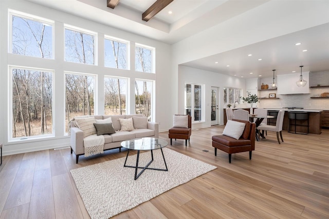 living room with a towering ceiling, baseboards, recessed lighting, light wood-style flooring, and beamed ceiling