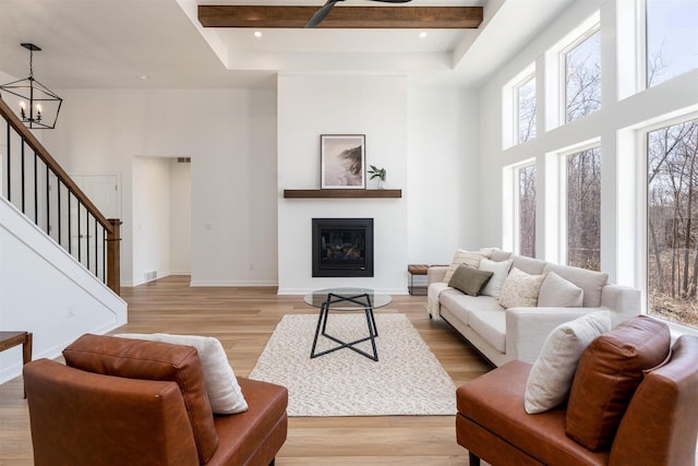 living area with light wood-style floors, beamed ceiling, a towering ceiling, stairs, and baseboards