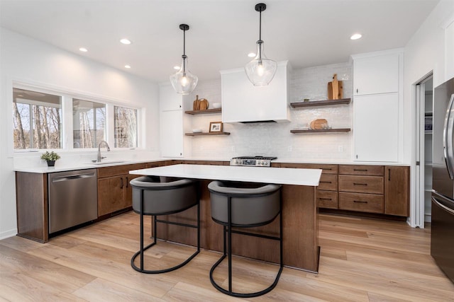 kitchen featuring stainless steel dishwasher, open shelves, a kitchen island, a sink, and light countertops