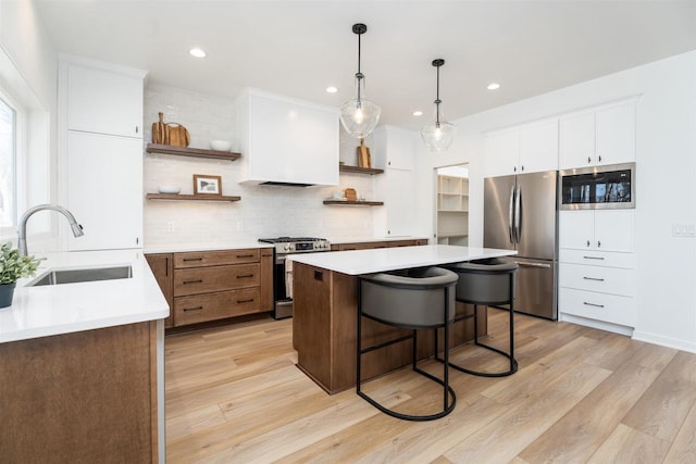 kitchen with open shelves, a sink, light countertops, a breakfast bar, and stainless steel appliances