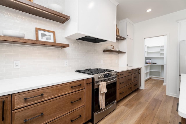 kitchen featuring stainless steel range with gas stovetop, light wood-type flooring, open shelves, premium range hood, and backsplash