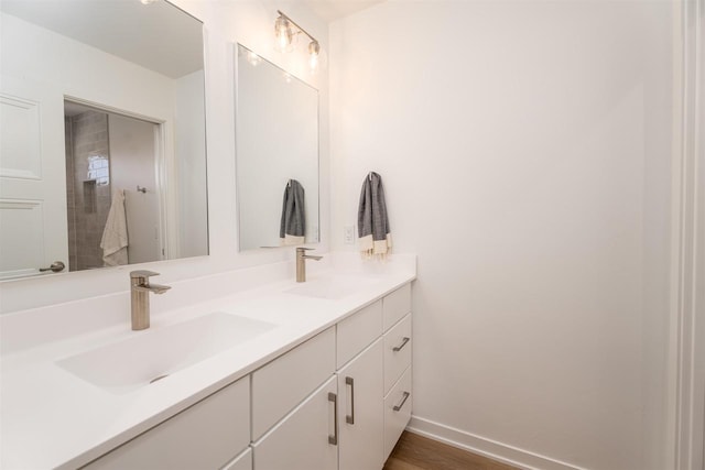 bathroom featuring wood finished floors, double vanity, a sink, and baseboards