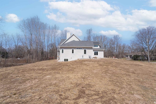 back of house with a yard, a chimney, and a shingled roof