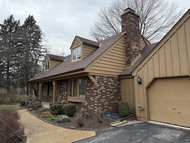 view of front of property featuring roof with shingles, a chimney, an attached garage, brick siding, and a porch