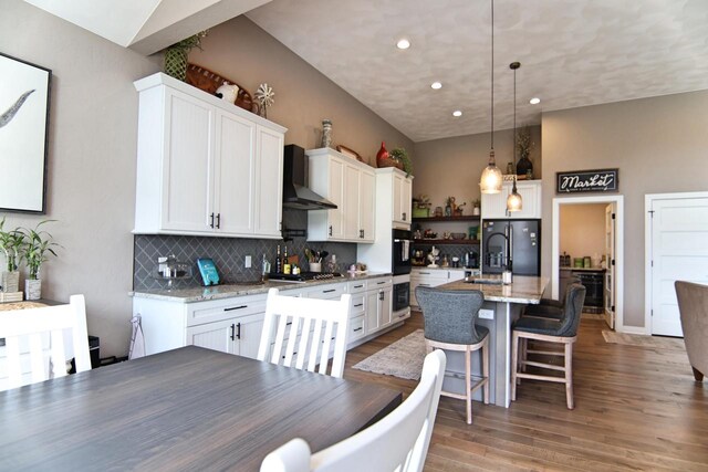 1817 Arboretum Dr, Janesville, WI 53548 - kitchen with wall chimney range hood, a breakfast bar, light wood-style floors, white cabinetry, and backsplash
