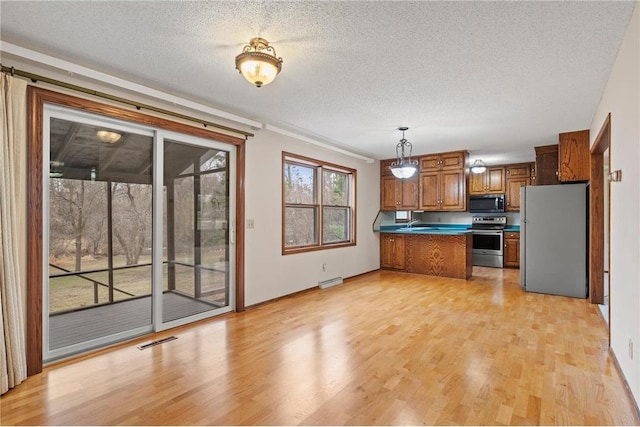 kitchen featuring brown cabinetry, stainless steel appliances, light wood finished floors, a peninsula, and visible vents