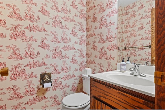 bathroom with toilet, vanity, and wallpapered walls