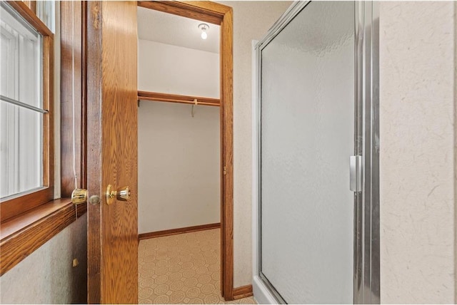 bathroom with baseboards, a spacious closet, and a stall shower