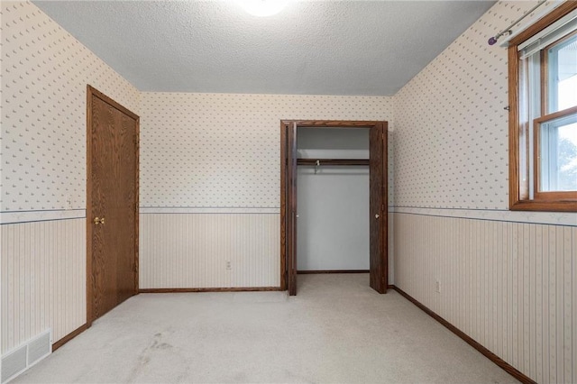 unfurnished bedroom with a wainscoted wall, wallpapered walls, and a closet