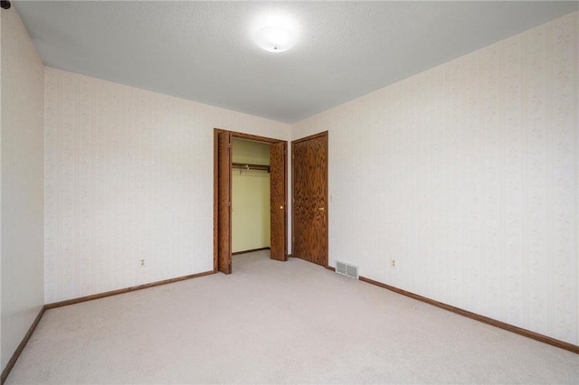 unfurnished bedroom featuring wallpapered walls, a closet, light colored carpet, baseboards, and visible vents