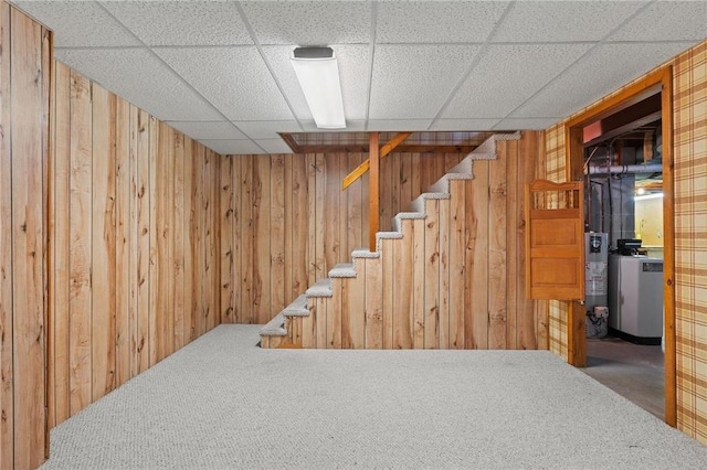 finished below grade area with a paneled ceiling, wood walls, carpet, and stairway