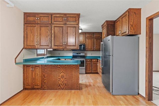 kitchen featuring stainless steel appliances, a sink, light wood-style floors, a peninsula, and brown cabinetry