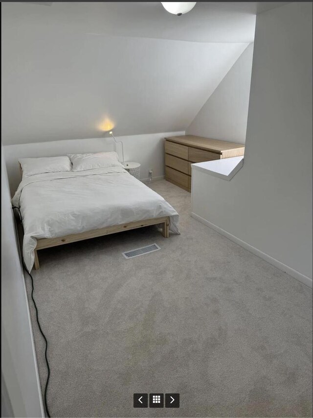 bedroom with baseboards, vaulted ceiling, and light carpet