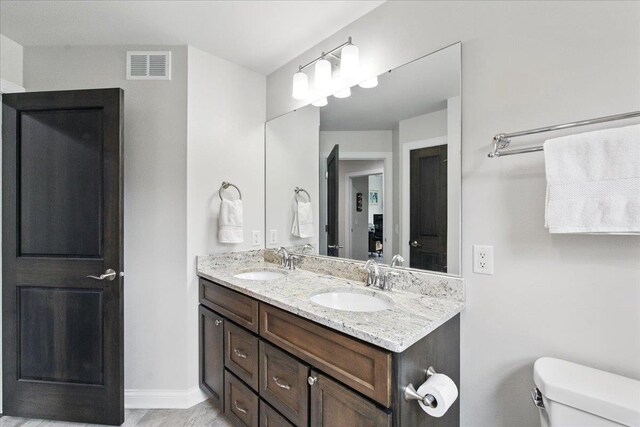 full bathroom with double vanity, toilet, visible vents, and a sink