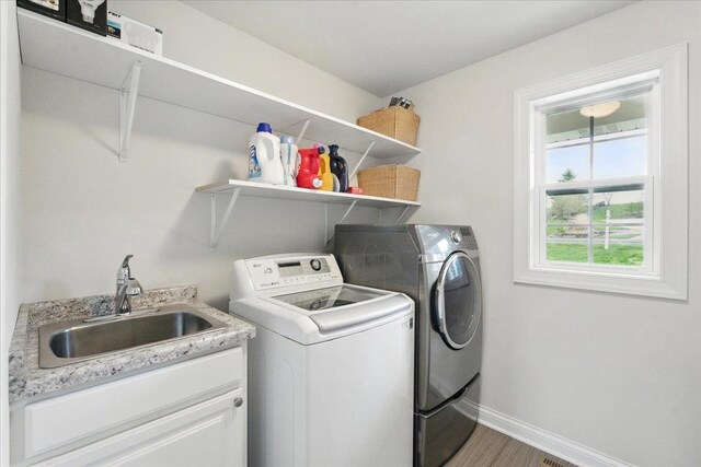 washroom with cabinet space, wood finished floors, a sink, baseboards, and washer and dryer