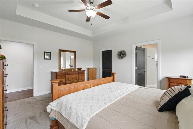 bedroom featuring a raised ceiling, carpet, a ceiling fan, baseboards, and ensuite bathroom