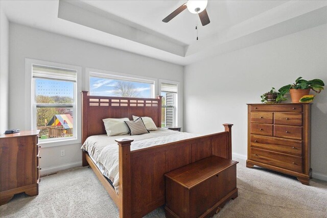 bedroom with ceiling fan, a tray ceiling, light colored carpet, and baseboards