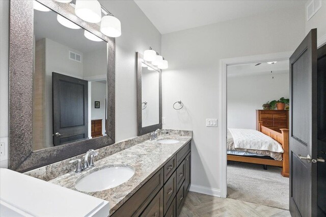 full bath featuring connected bathroom, double vanity, visible vents, and a sink