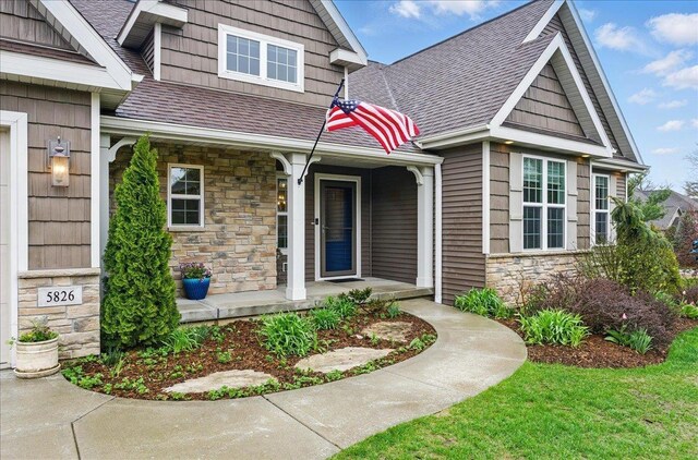 doorway to property featuring roof with shingles, covered porch, and stone siding