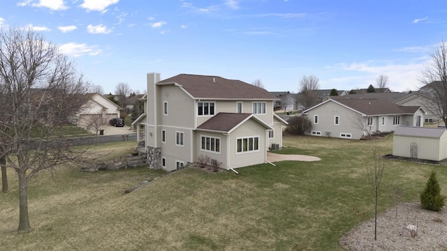 rear view of house featuring a residential view, a chimney, an outdoor structure, a yard, and a shed