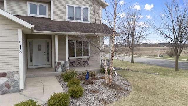 doorway to property featuring a lawn, a porch, and a shingled roof