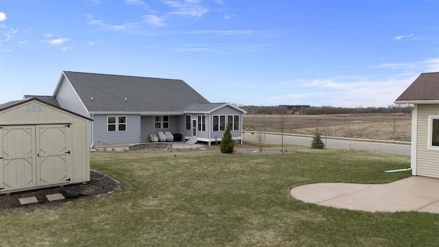 back of property featuring a storage shed, a patio area, a lawn, a shingled roof, and an outdoor structure