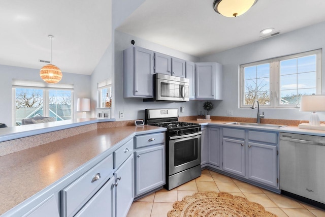 kitchen featuring light tile patterned floors, gray cabinetry, appliances with stainless steel finishes, a sink, and hanging light fixtures